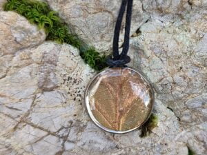 Obesek z listom bukve in črno bombažno vrvico na kamnu.